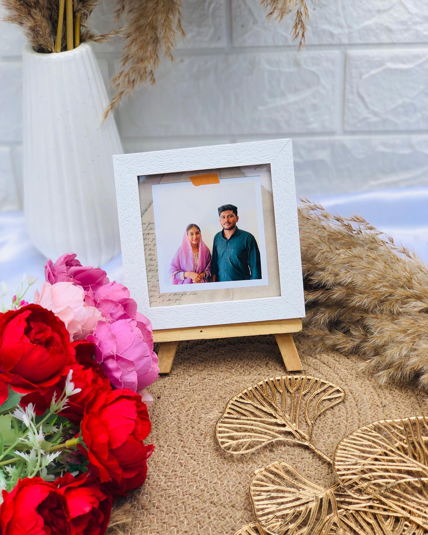 A personalized couple portrait in a textured white frame, styled with pastel roses and dried pampas grass.