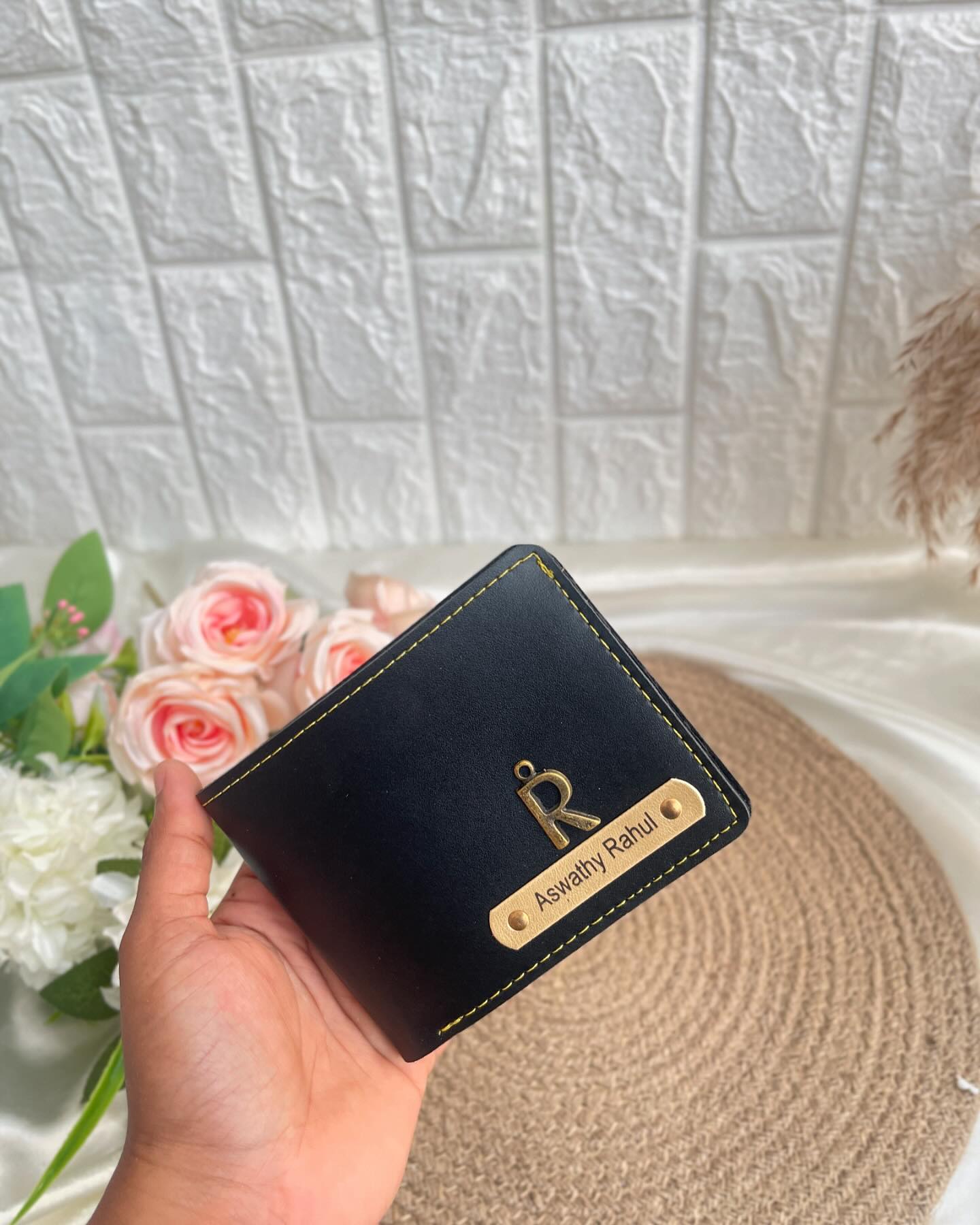 A sleek name-engraved leather wallet presented alongside a soft bouquet of blush roses.