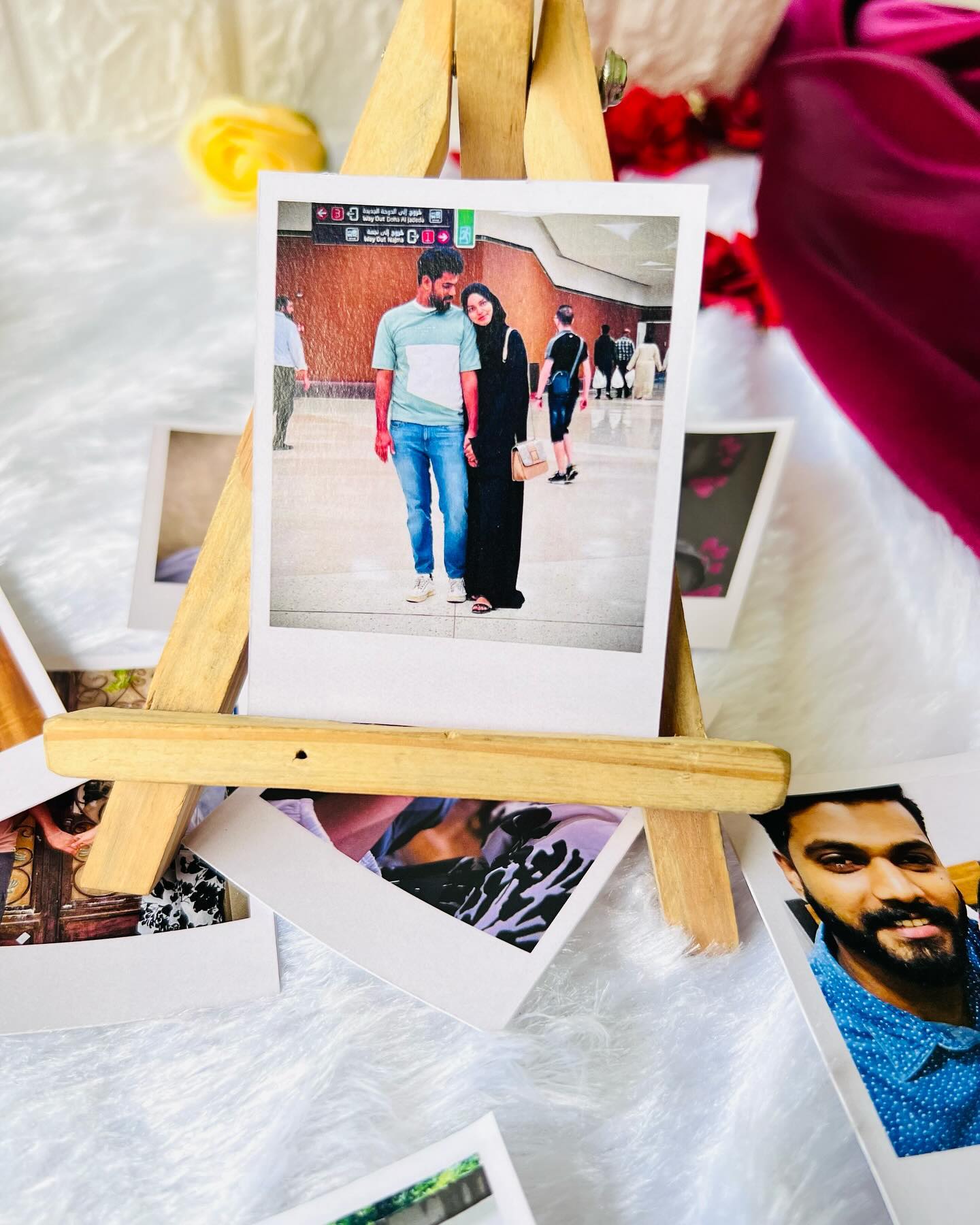 A romantic bundle of personalized polaroid photo prints styled with red roses, gold leaf sprigs, and a satin drape for an elegant anniversary surprise.