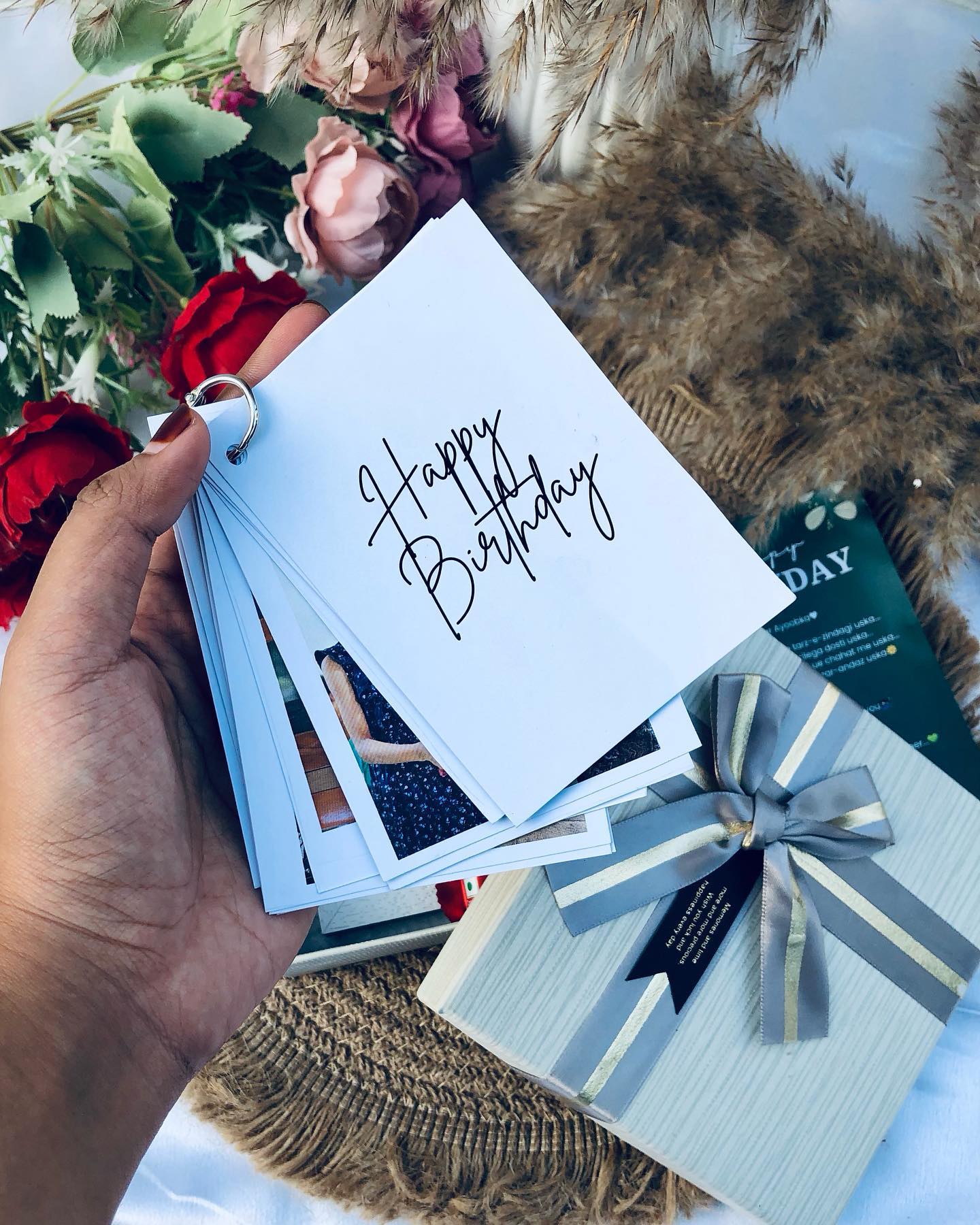 A hand-tied rose bouquet paired with a ring-bound photo flip book that spells out Happy Birthday and a ribboned keepsake box.