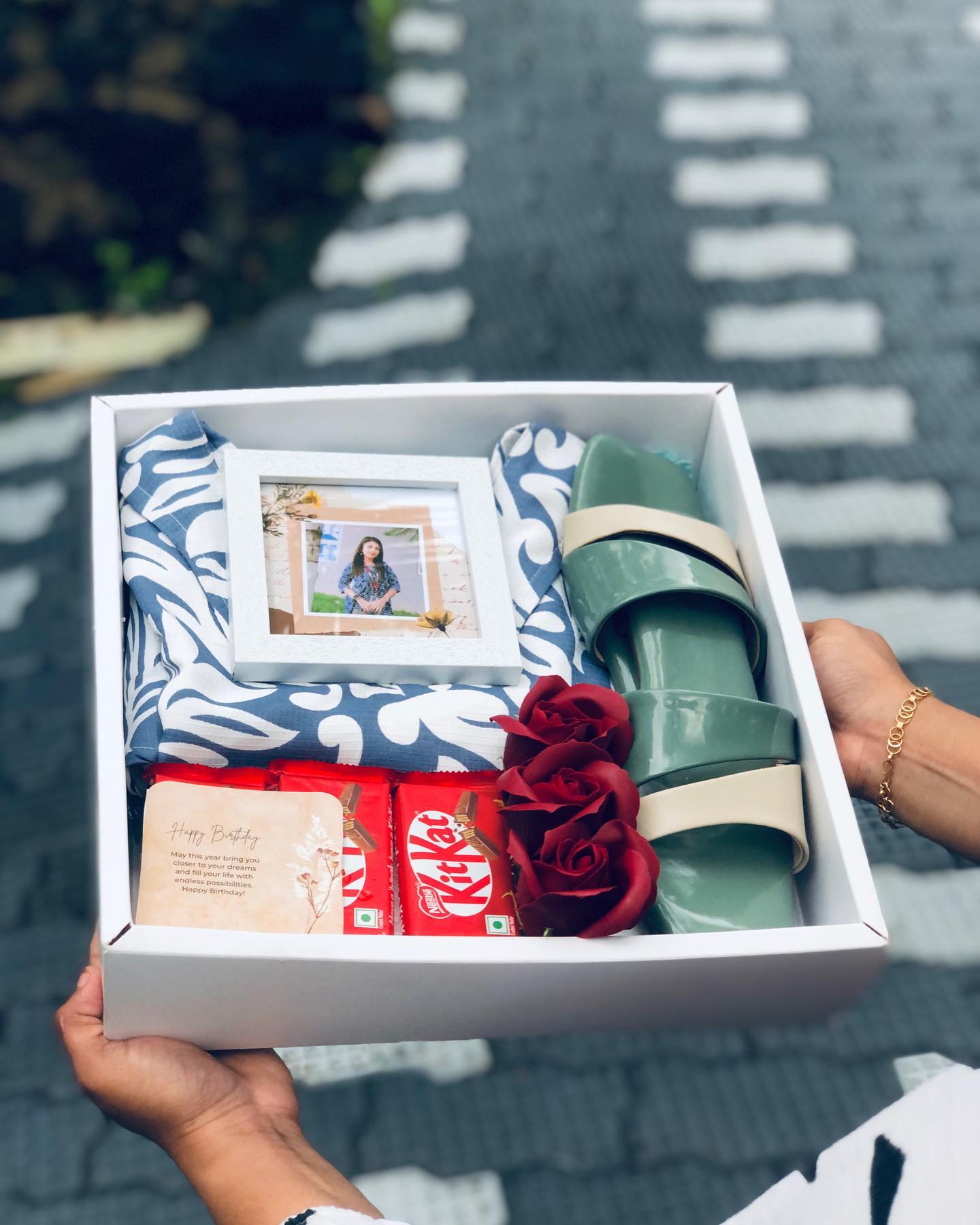 An elegant birthday gift box with a printed keepsake, chocolates, silk-look scarf, red roses, and stylish sandals.