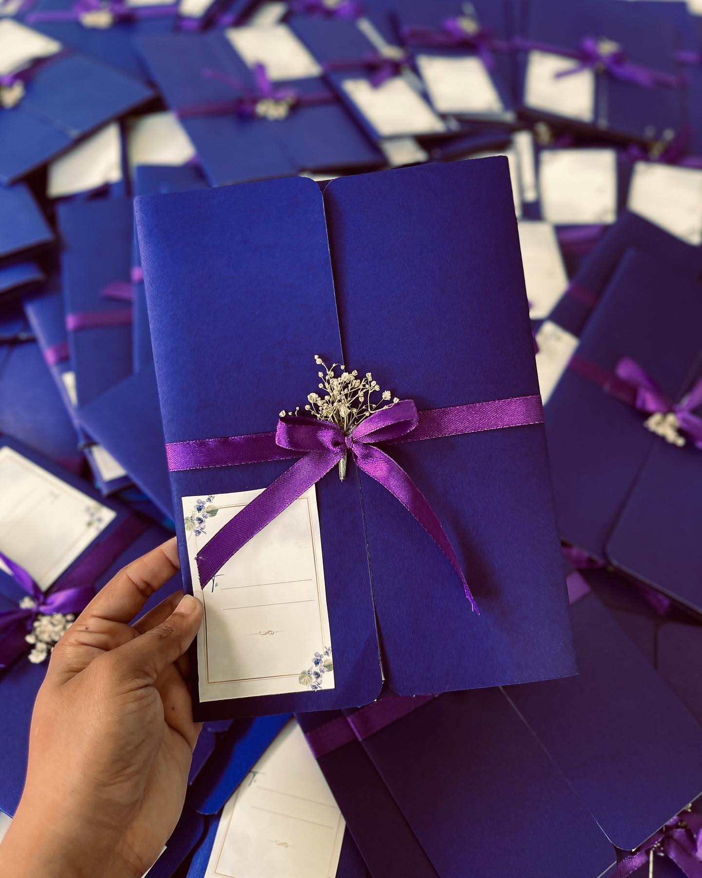 A sleek navy gift box finished with a satin purple bow, dried baby's breath, and a keepsake to-and-from tag.