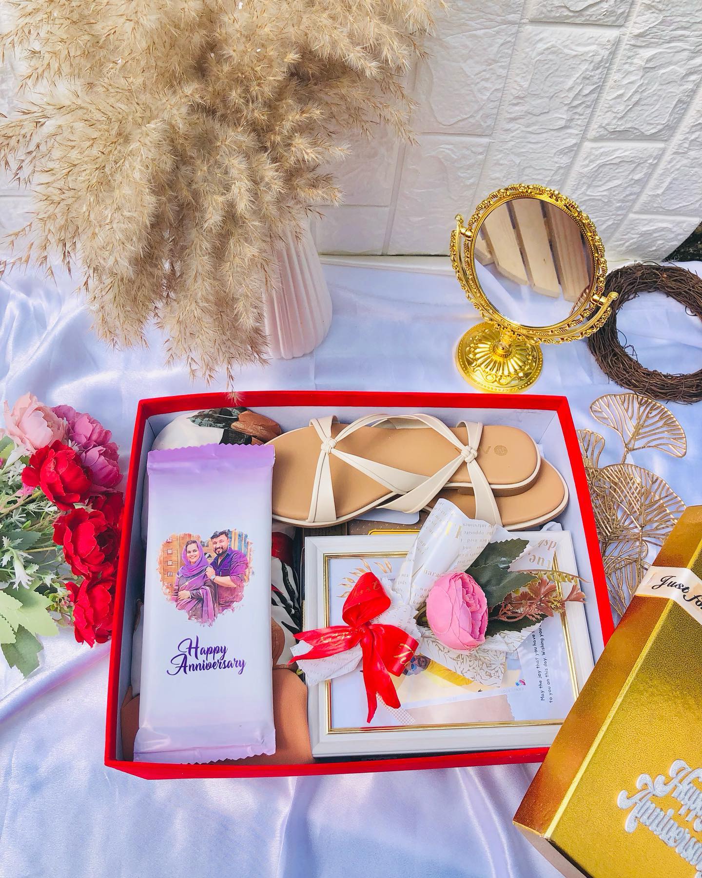 A generous anniversary hamper with strappy sandals, a gilded vanity mirror, a personalized photo chocolate, and a keepsake card.
