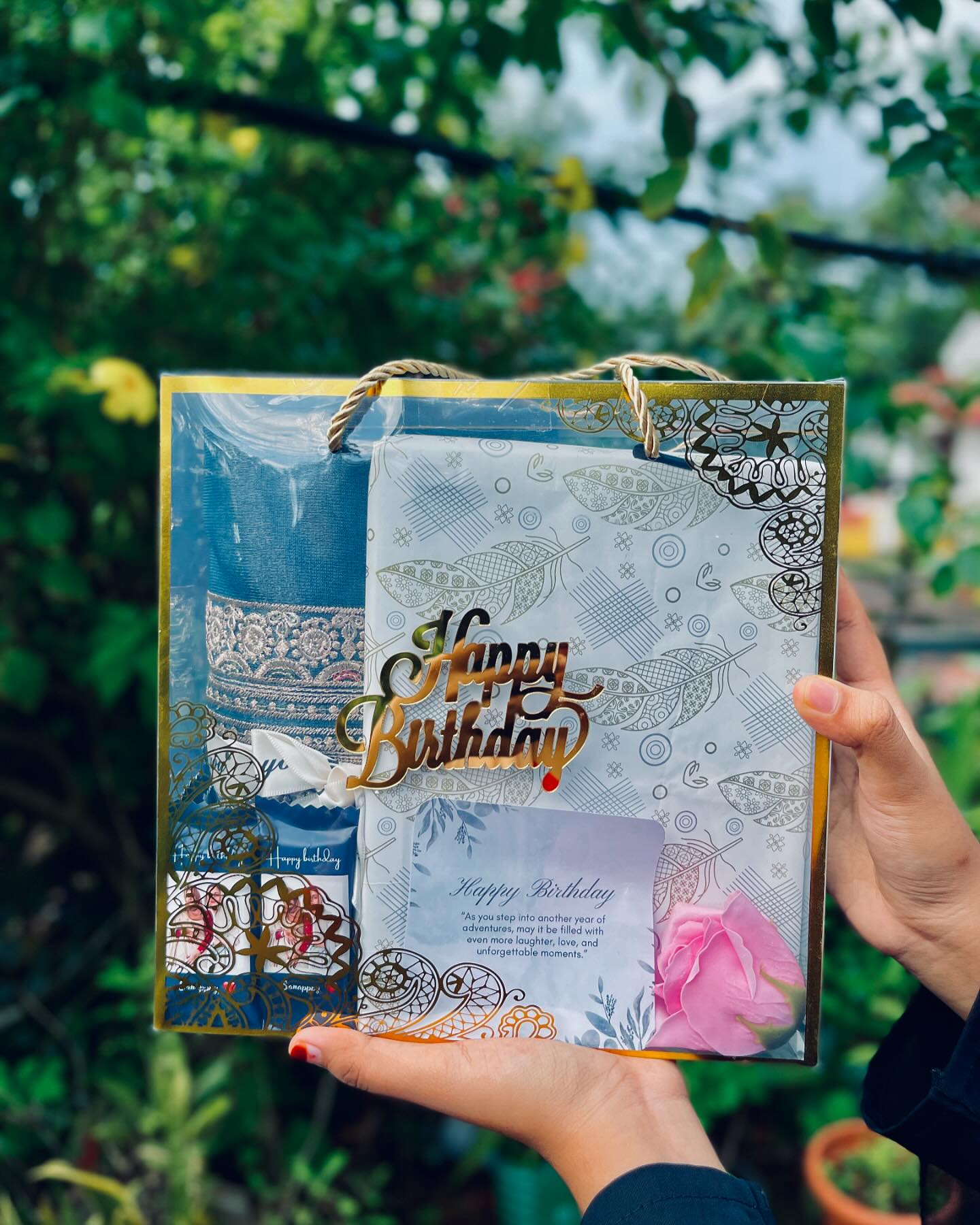 A festive gift bag featuring an embroidered saree, a heartfelt birthday card, and a fresh pink rose.