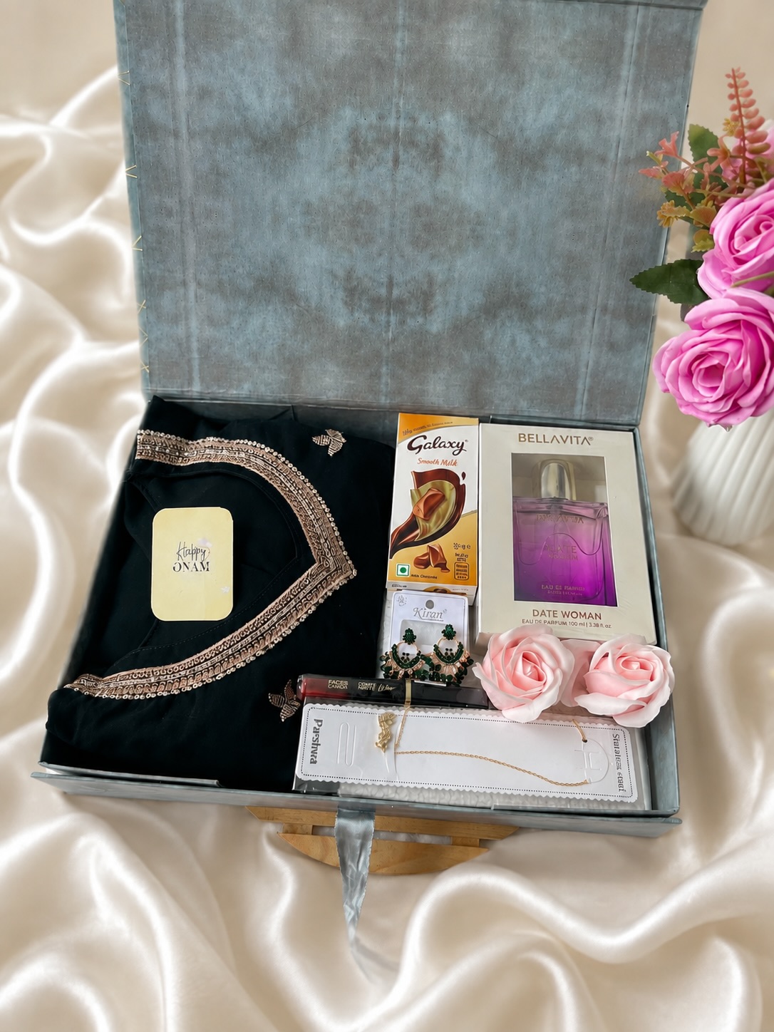 An elegant festive hamper with an embellished black saree, perfume, jewelry, lipstick, and chocolates.