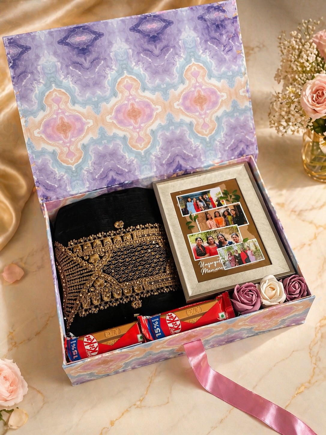 An elegant marbled gift box pairing an embroidered black saree with a personalized 'Unforgettable Memories' photo frame and KitKat bars.