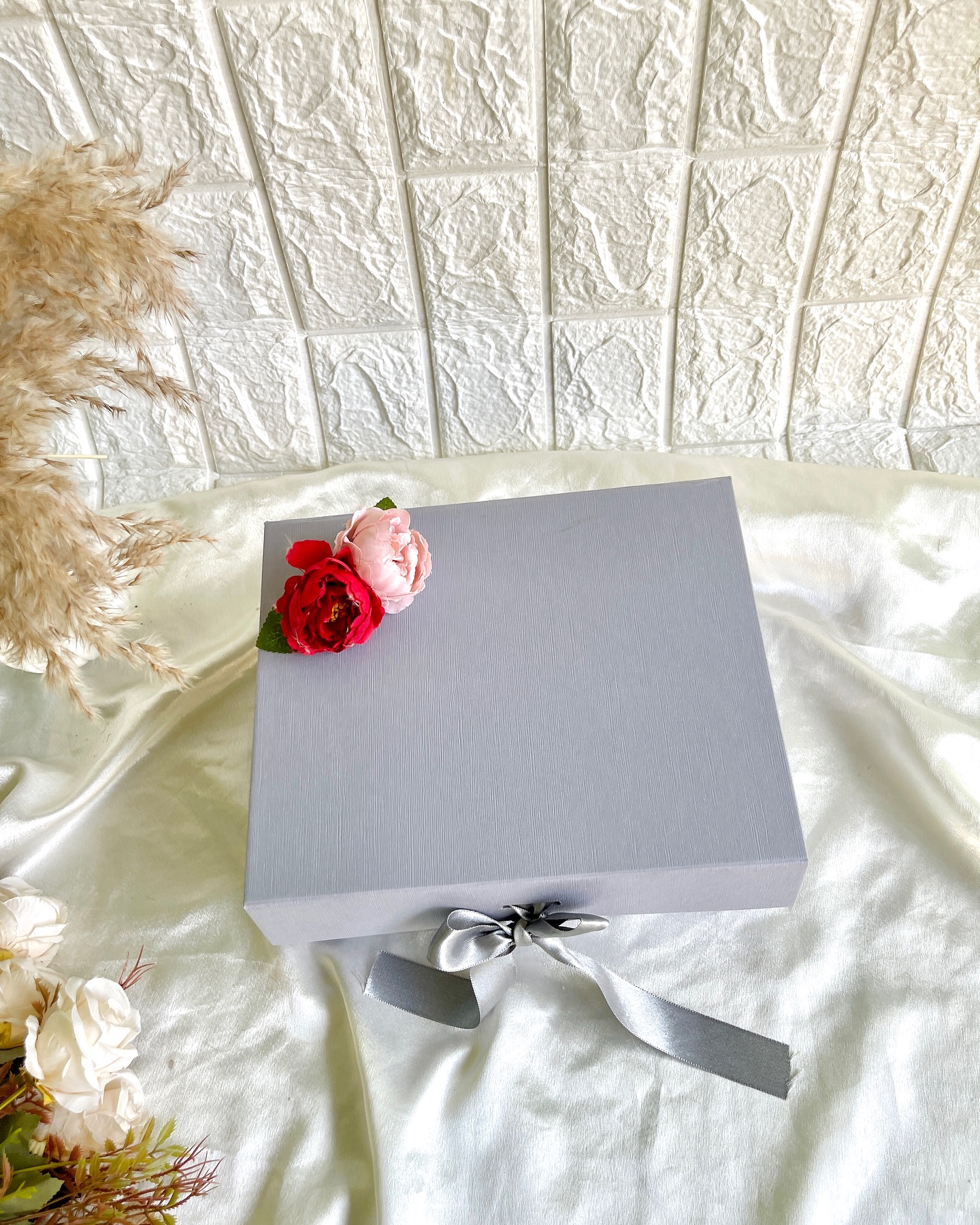 An elegant silver-grey gift box adorned with fresh roses and a satin ribbon bow.