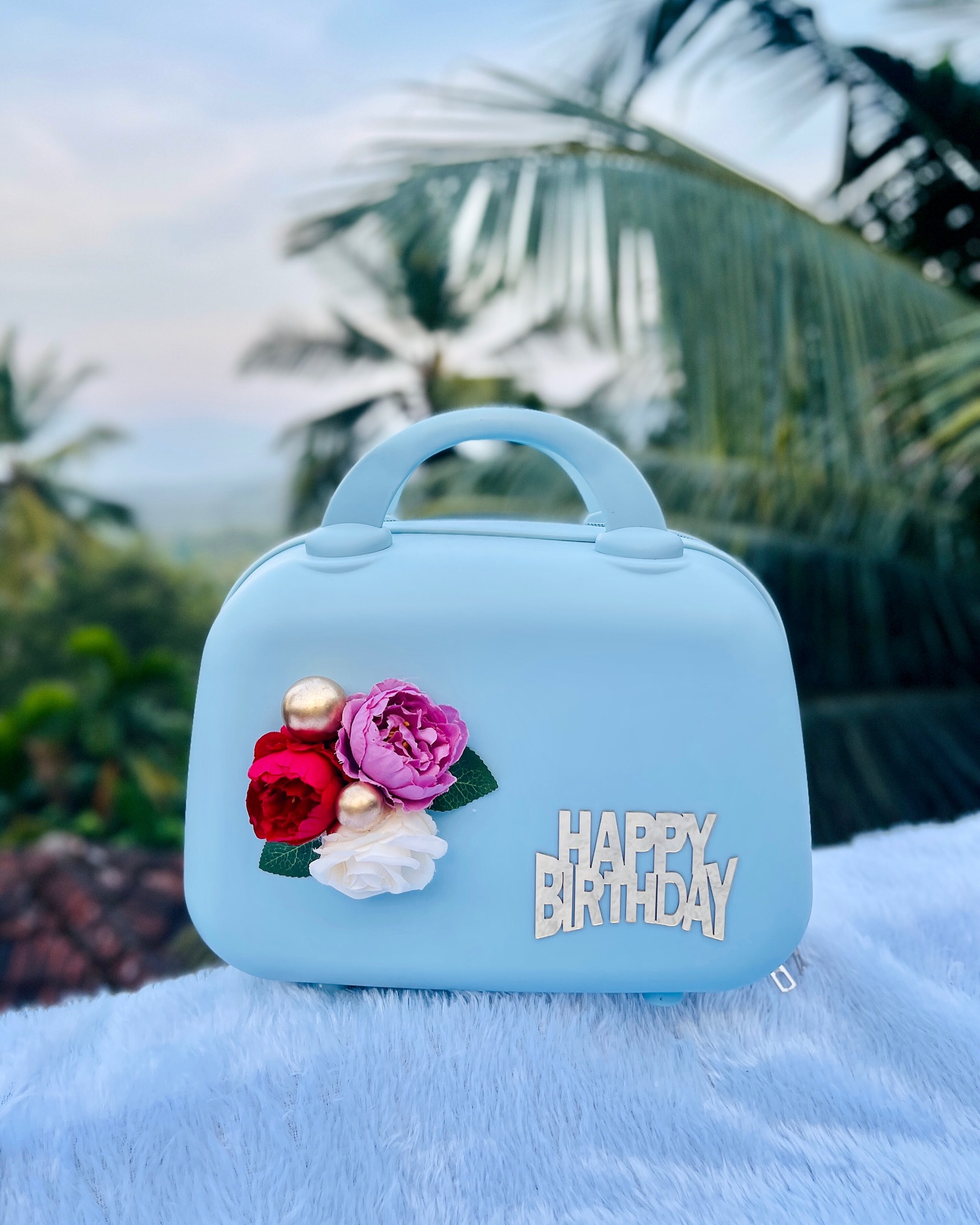 A powder blue vanity case decorated with silk roses and a Happy Birthday topper, doubling as a keepsake bag.