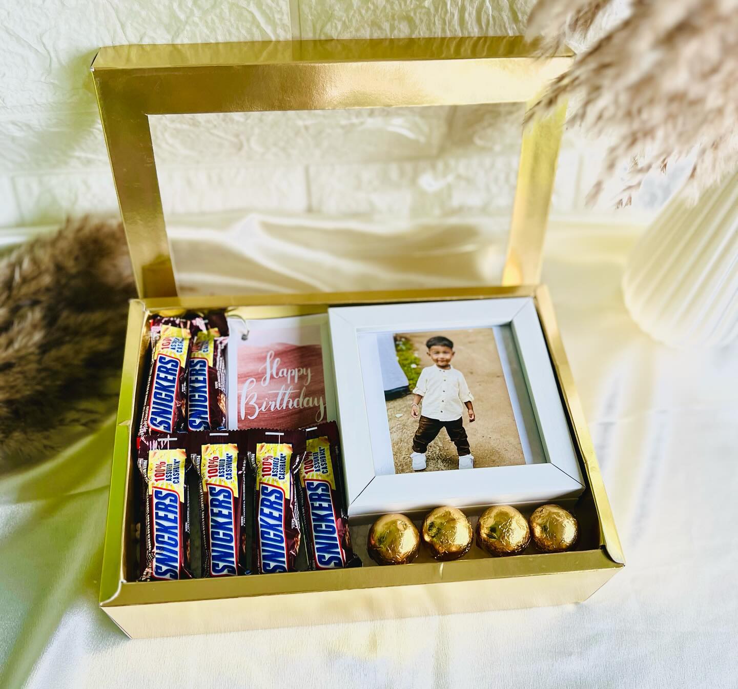 A gold birthday hamper filled with Snickers bars, gold-wrapped chocolate truffles and a personalized mini photo frame.