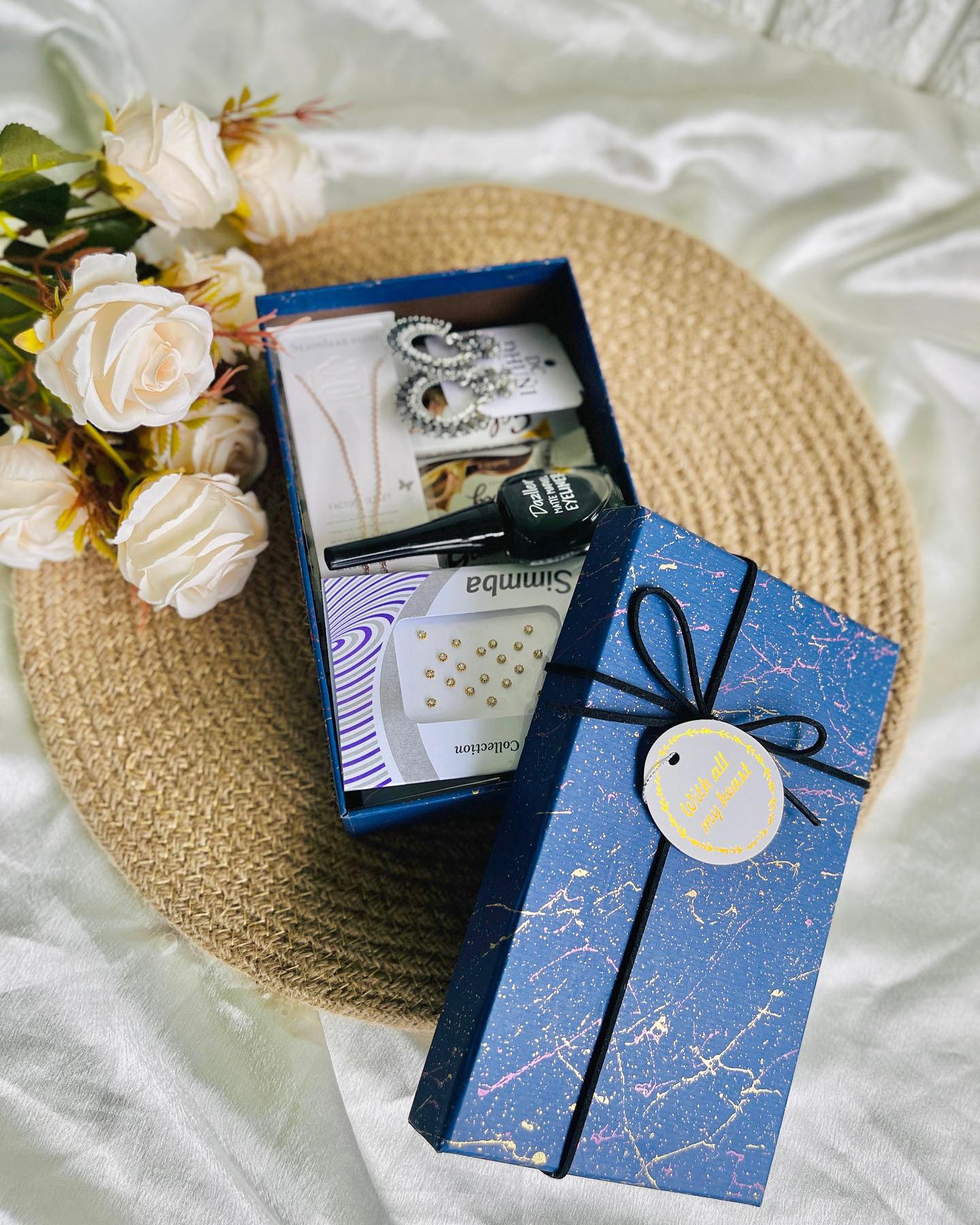 A navy keepsake box loaded with statement earrings, a necklace, eyeliner, nose pins, and a hair curler.