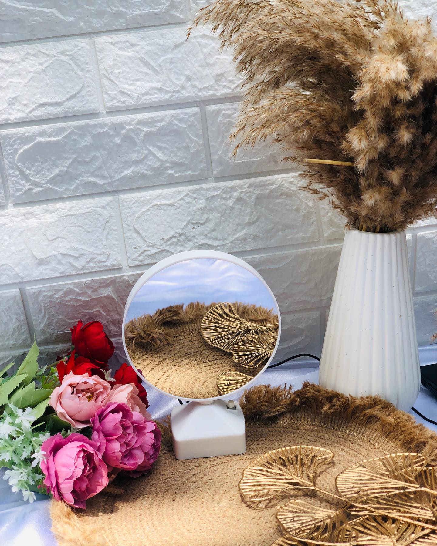A round decorative mirror lamp with a sunset-scene backdrop, styled with dried pampas grass, roses and gold leaf coasters.
