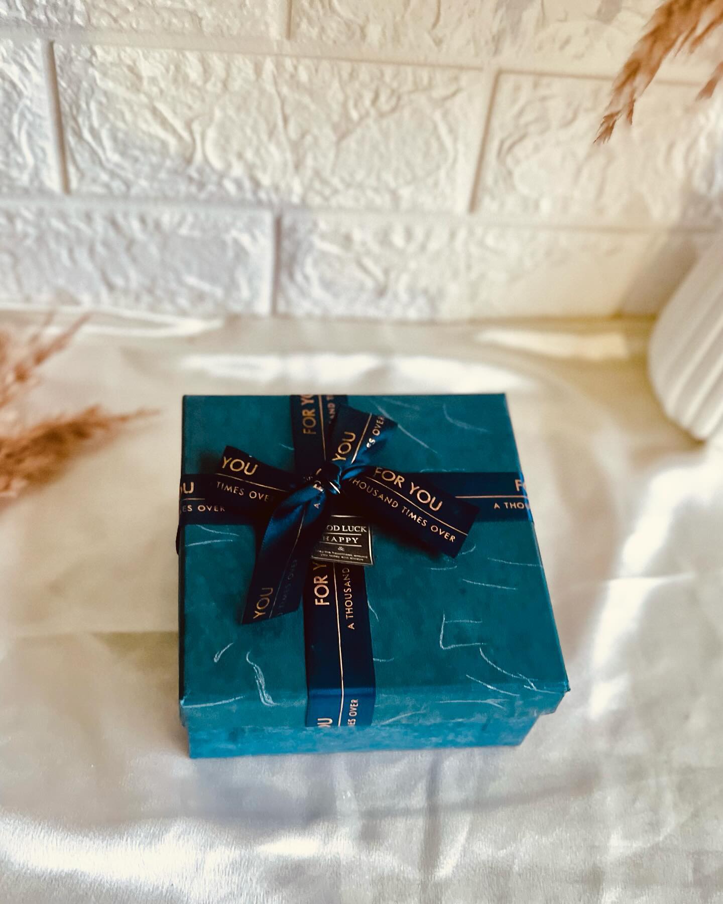 A teal marble-wrapped gift box tied with a navy "For You" ribbon and a Good Luck & Happy tag.