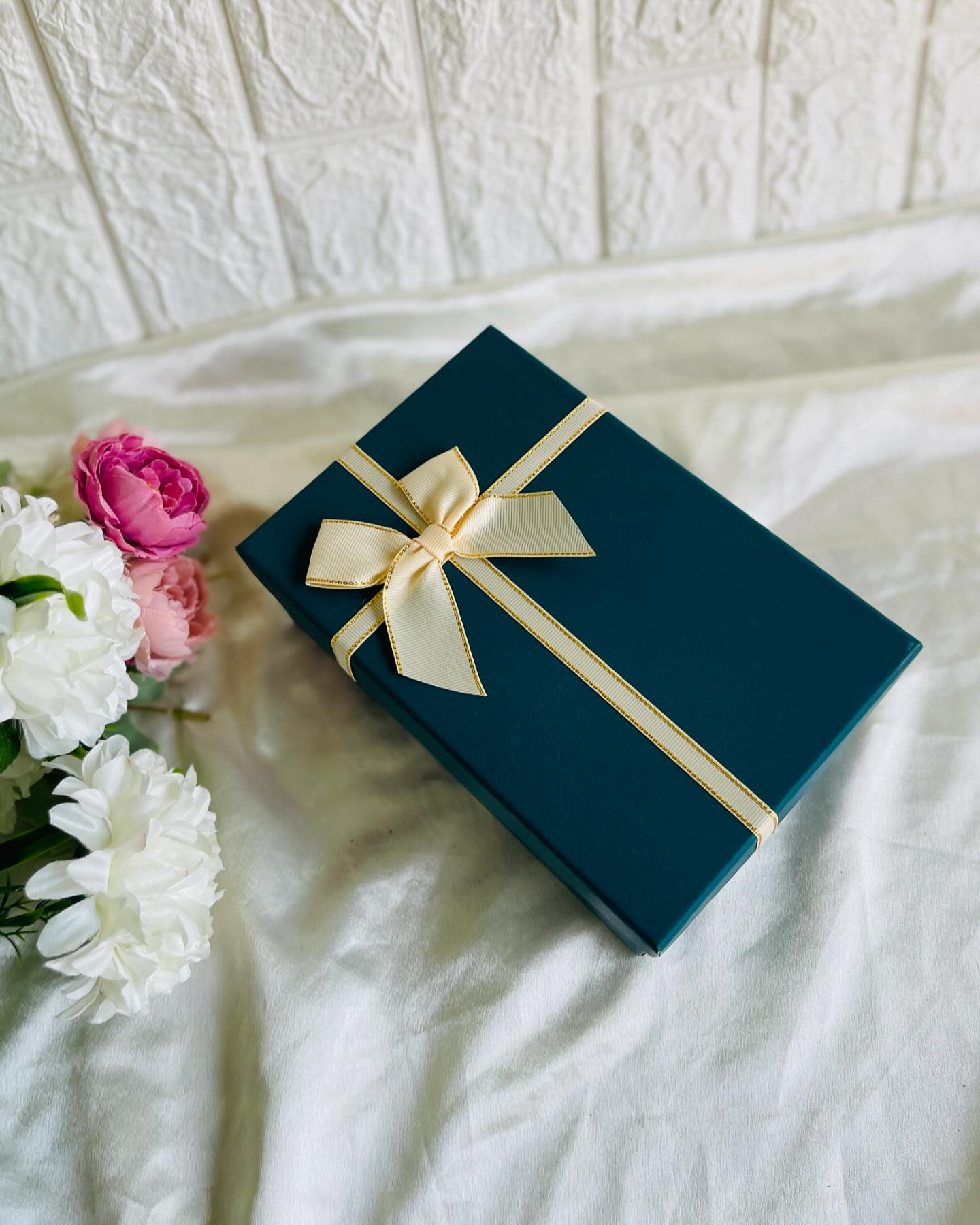 An elegant teal gift box tied with a satin cream bow, styled alongside fresh pink and white roses.