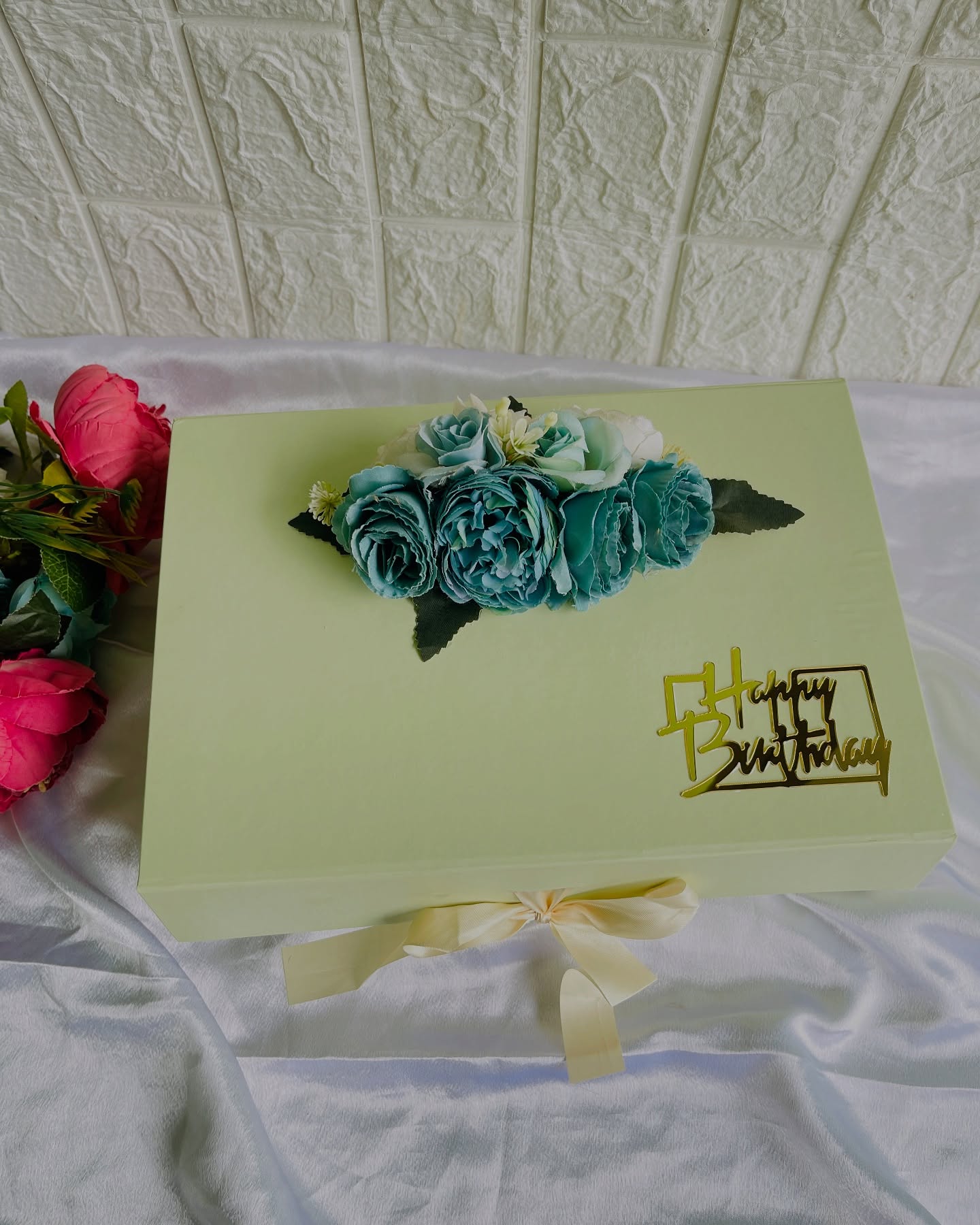 A soft sage gift box crowned with a lush teal rose bouquet and a gold Happy Birthday topper.