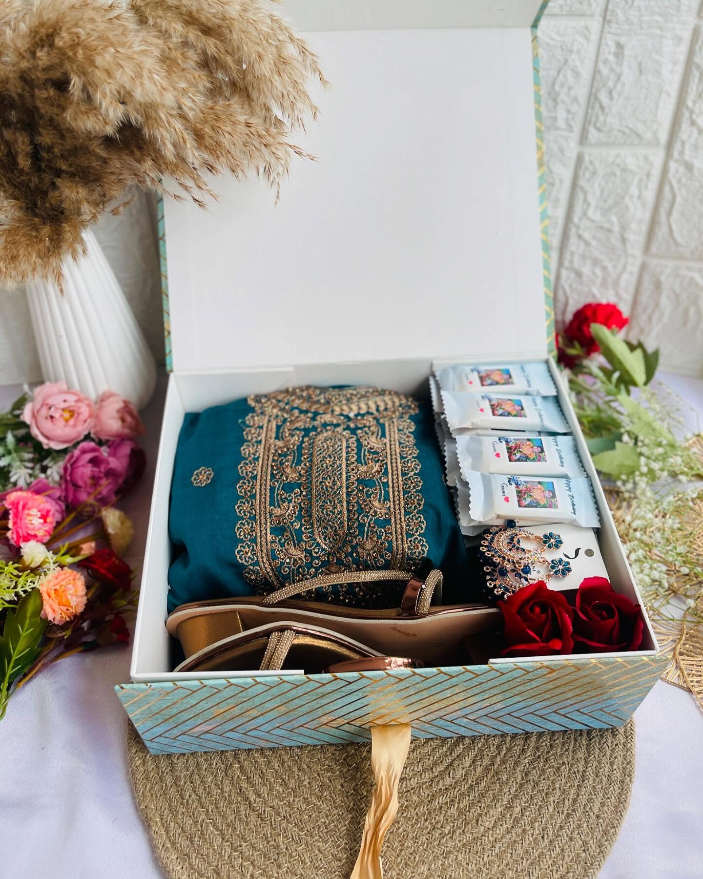 An elegant birthday hamper with an embroidered teal saree, gold sandals, earrings, and chocolates.