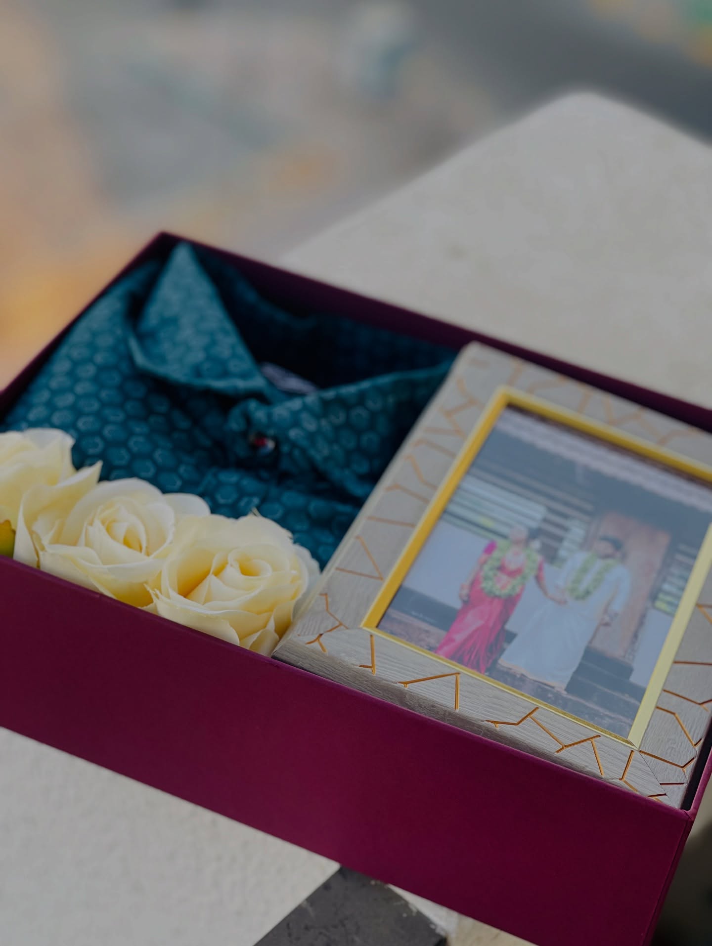 A wine-red gift box pairing a teal print shirt with a personalized couple photo frame and soft cream roses.