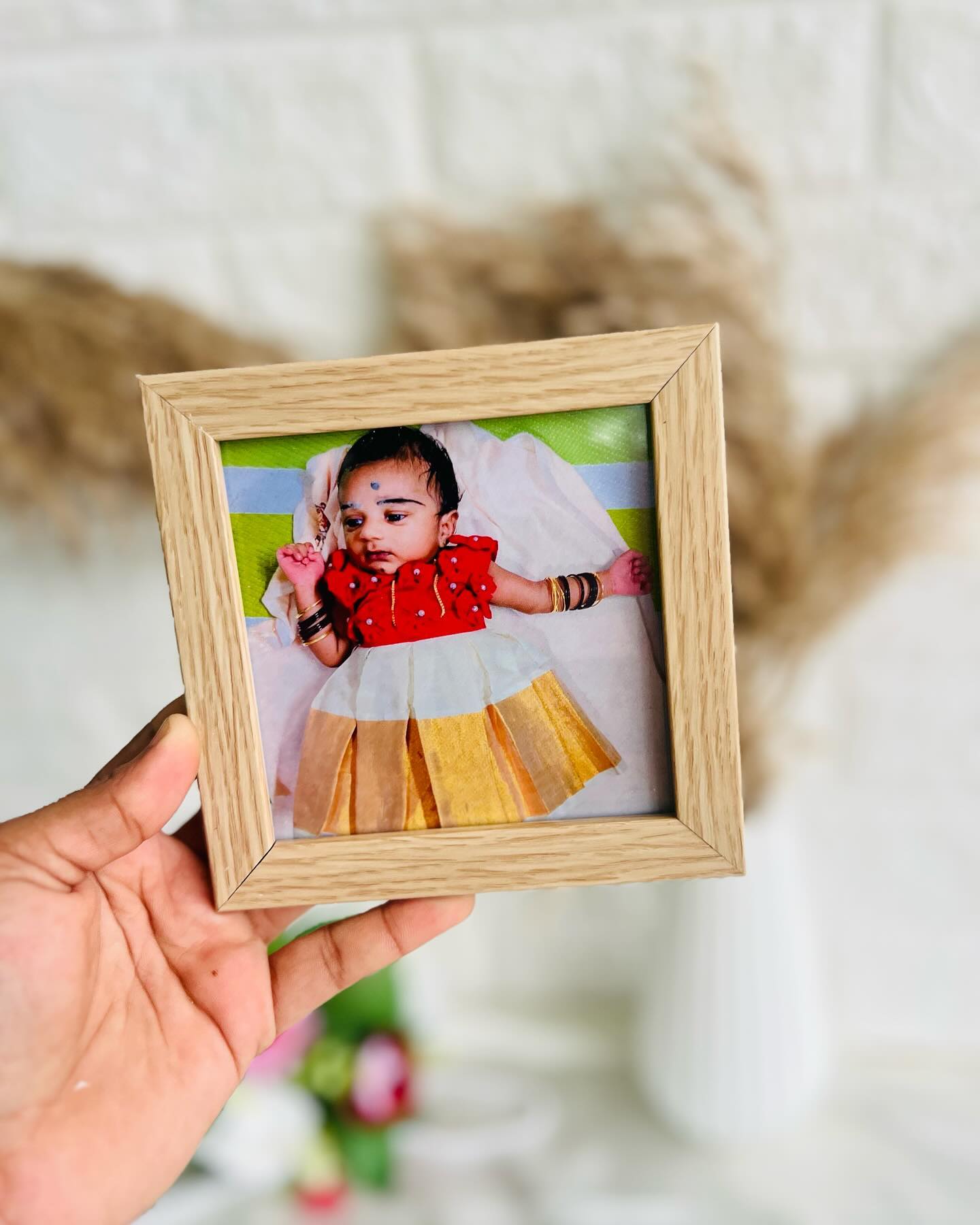 A warm wooden-finish photo frame capturing a baby in traditional red and gold attire.
