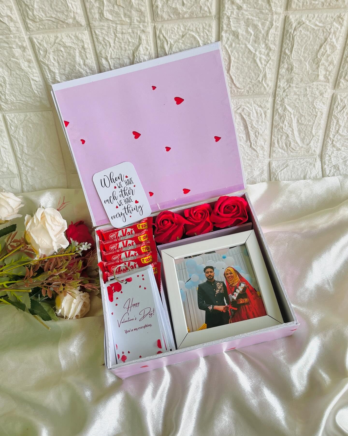 A romantic gift box with a personalized couple photo frame, red roses and Kitkat chocolates.