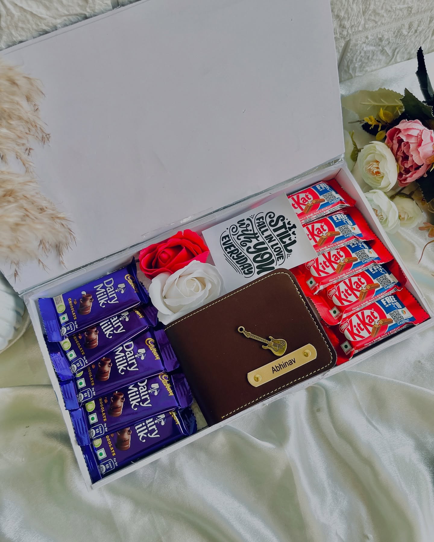 A personalized brown leather wallet nestled with Cadbury Dairy Milk, KitKat bars and roses for someone still falling in love with you every day.