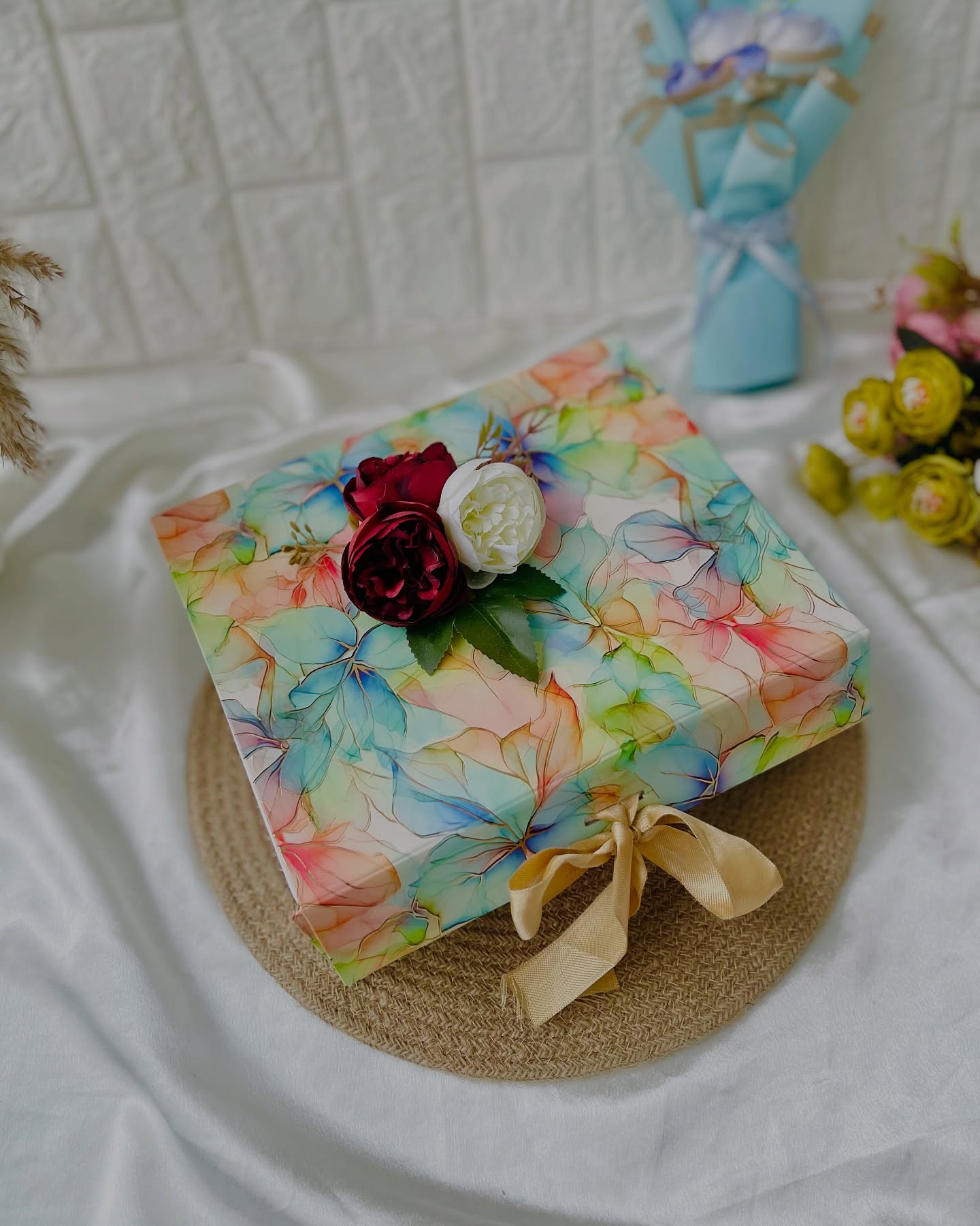 A watercolor-print gift box crowned with a deep red and ivory rose duo, tied with a golden ribbon.