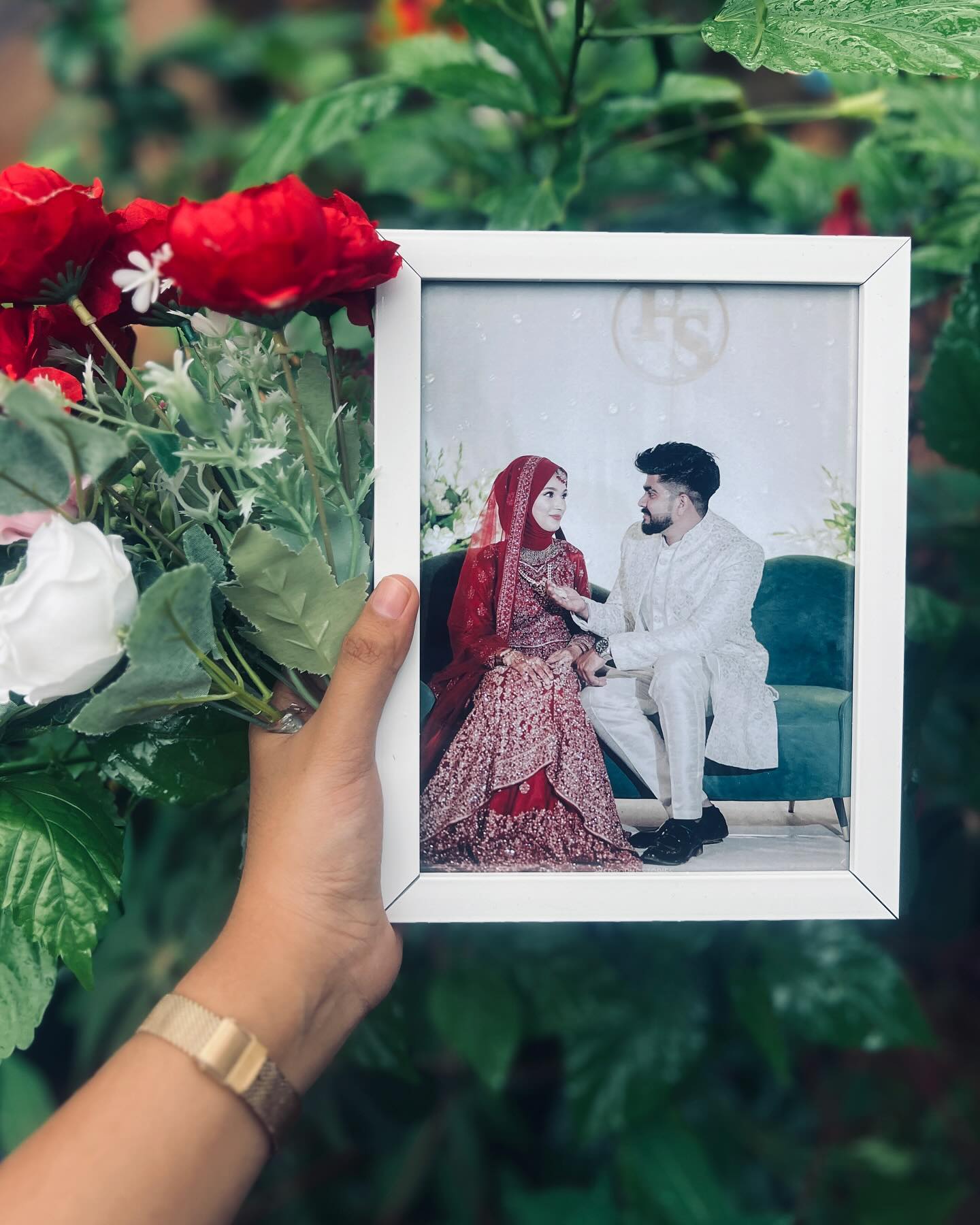 A white-framed wedding portrait held amid red and white blooms, perfect as a lasting keepsake.