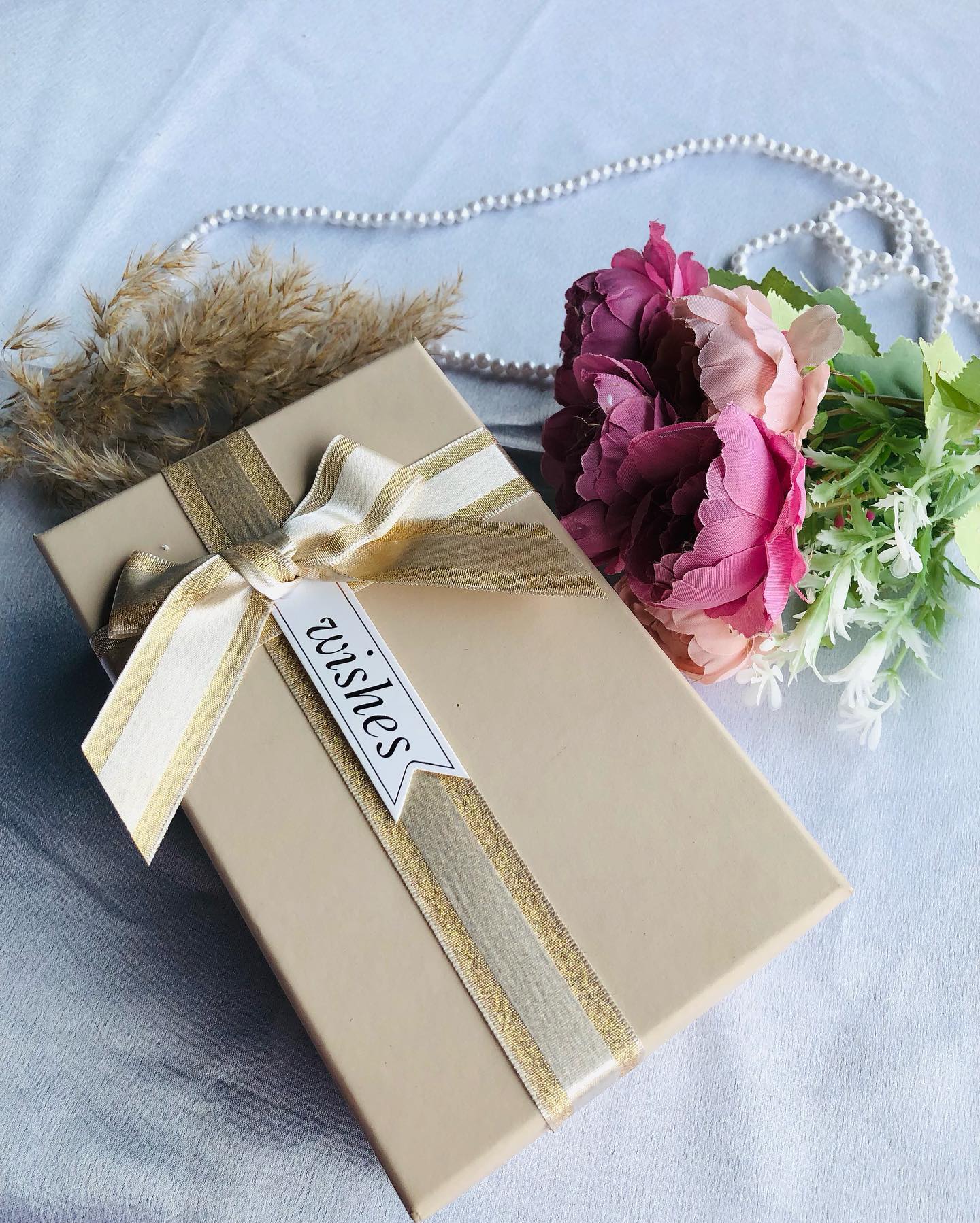 A cream gift box tied in gold-striped ribbon with a "Wishes" tag and matching birthday greeting card.