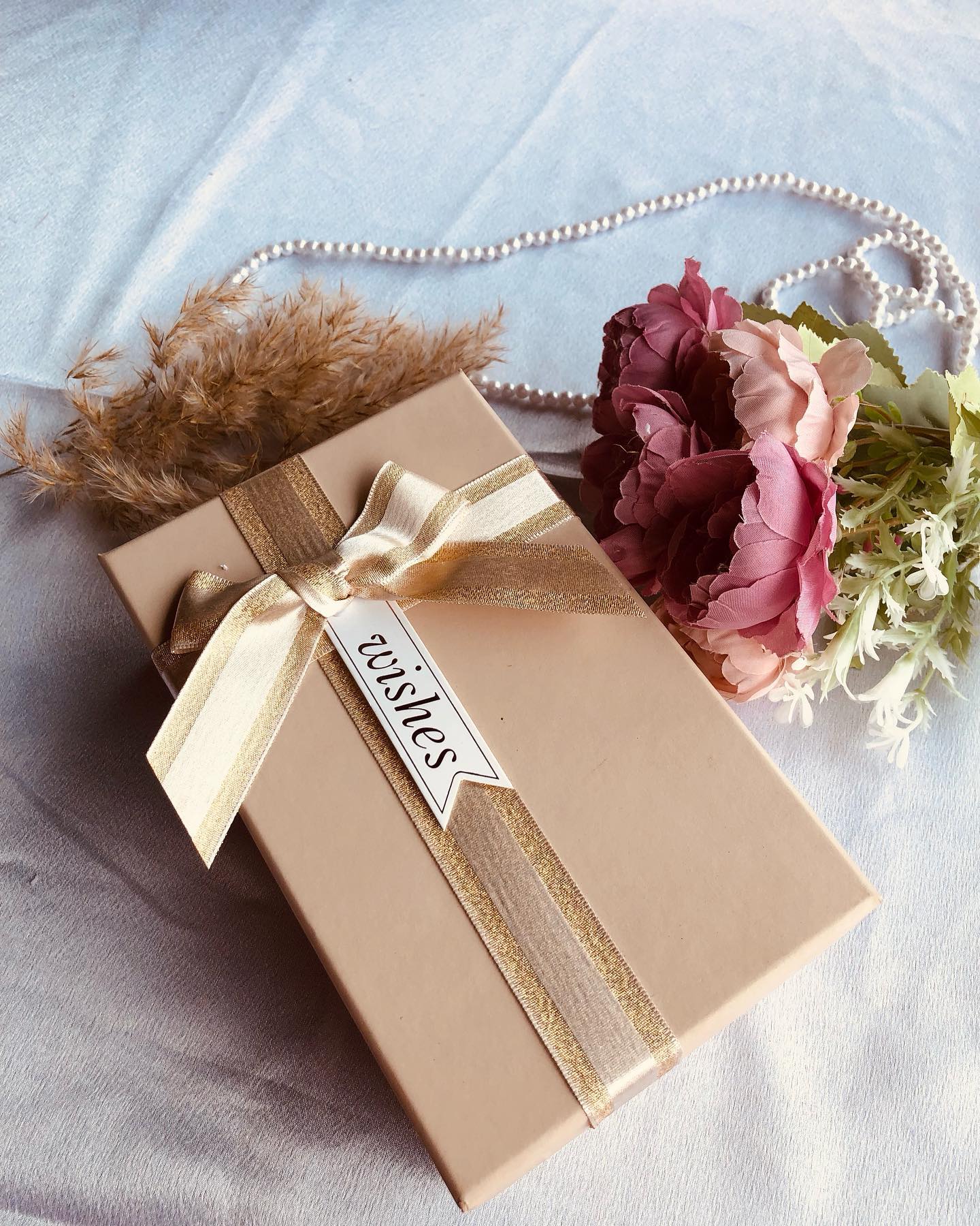 An elegantly kraft-wrapped gift box finished with a shimmering gold ribbon bow and a 'wishes' tag.